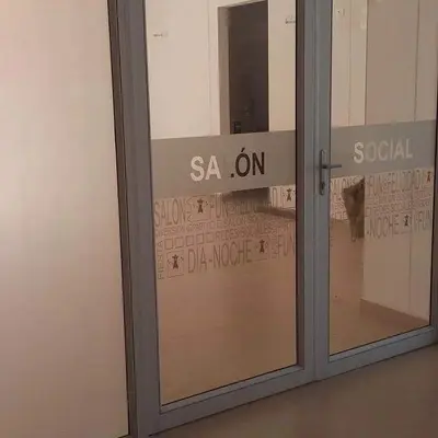 Puerta de acceso de vidrio templado al Salón Social con vinilos decorativos.