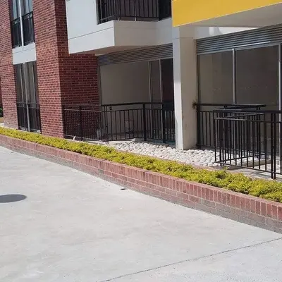 Sendero peatonal exterior rodeado de jardineras de ladrillo y plantas decorativas.