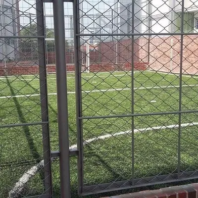 Cancha sintética de fútbol cercada con malla metálica para recreación.